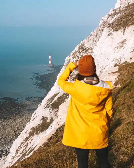 junge Frau schaut auf den Leuchtturm von den Klippen aus an Beachy Head in England