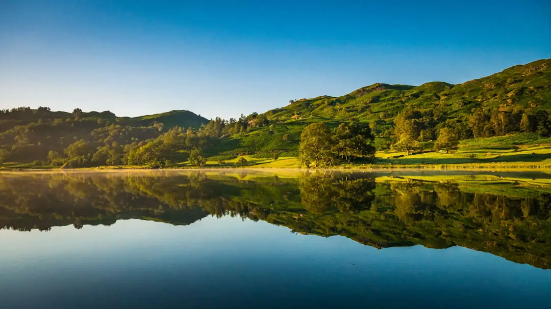 Blick auf einen See im Lake District in England mit grünen Hügeln dahinter