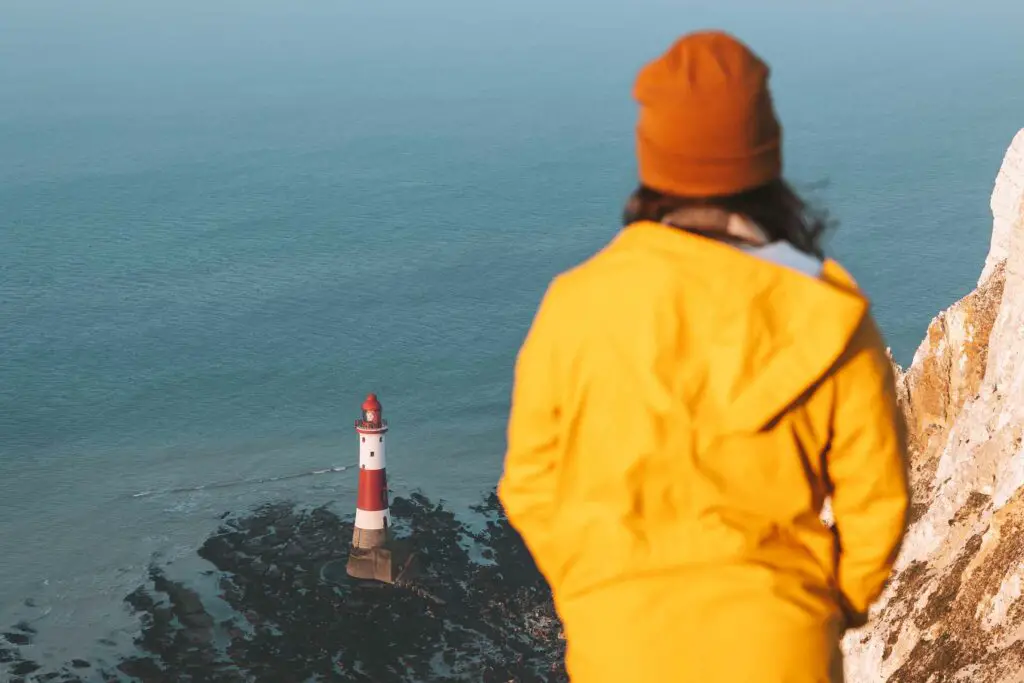 junge Frau an der Küste des Beachy Head in England mit Leuchtturm im Hintergrund