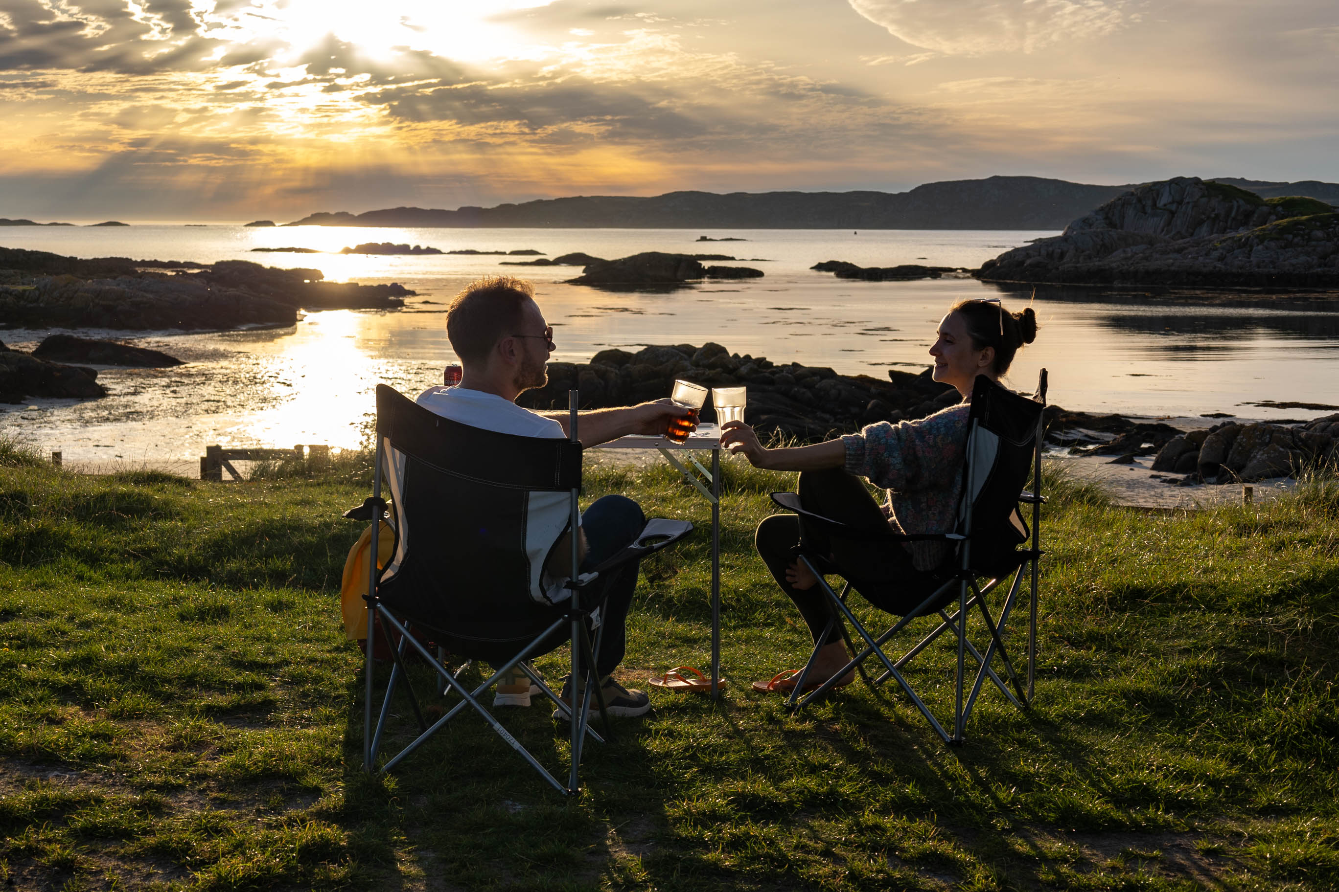 junge Leute sitzen auf dem Campingplatz Fidden Farm Campsite in Schottland und blicken auf das Meer