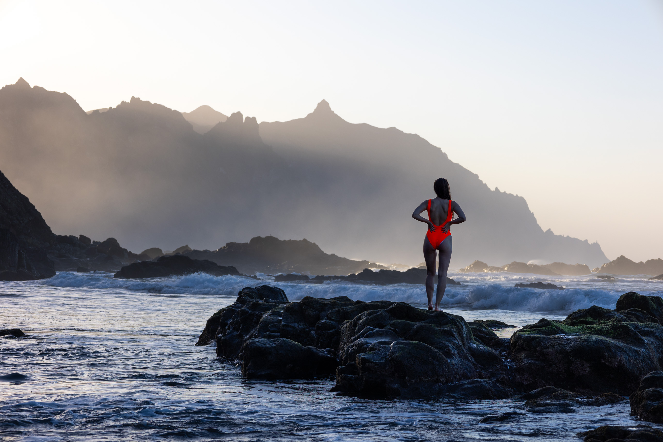 junge Frau auf Felsen am schwarzen Sandstrand auf Teneriffa